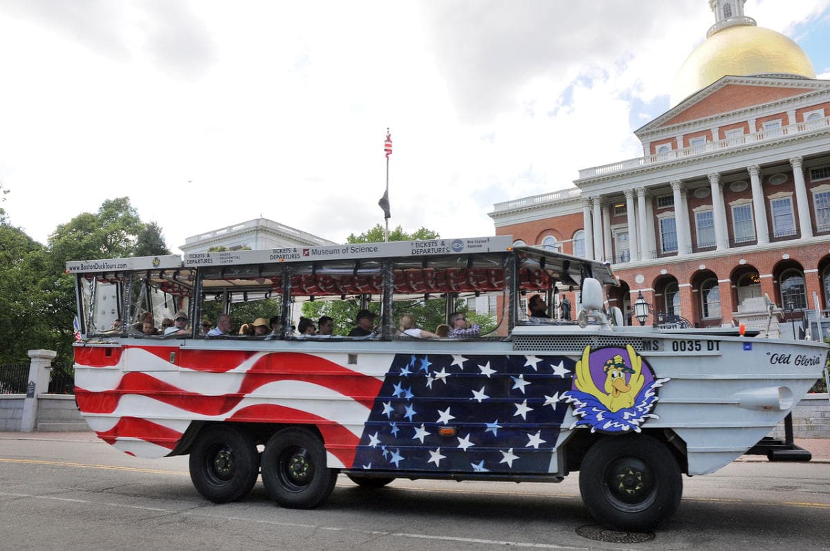 A stars-and-stripes Boston Duck Tours amphibious vehicle on the street outside the gold-domed Massachusetts State House